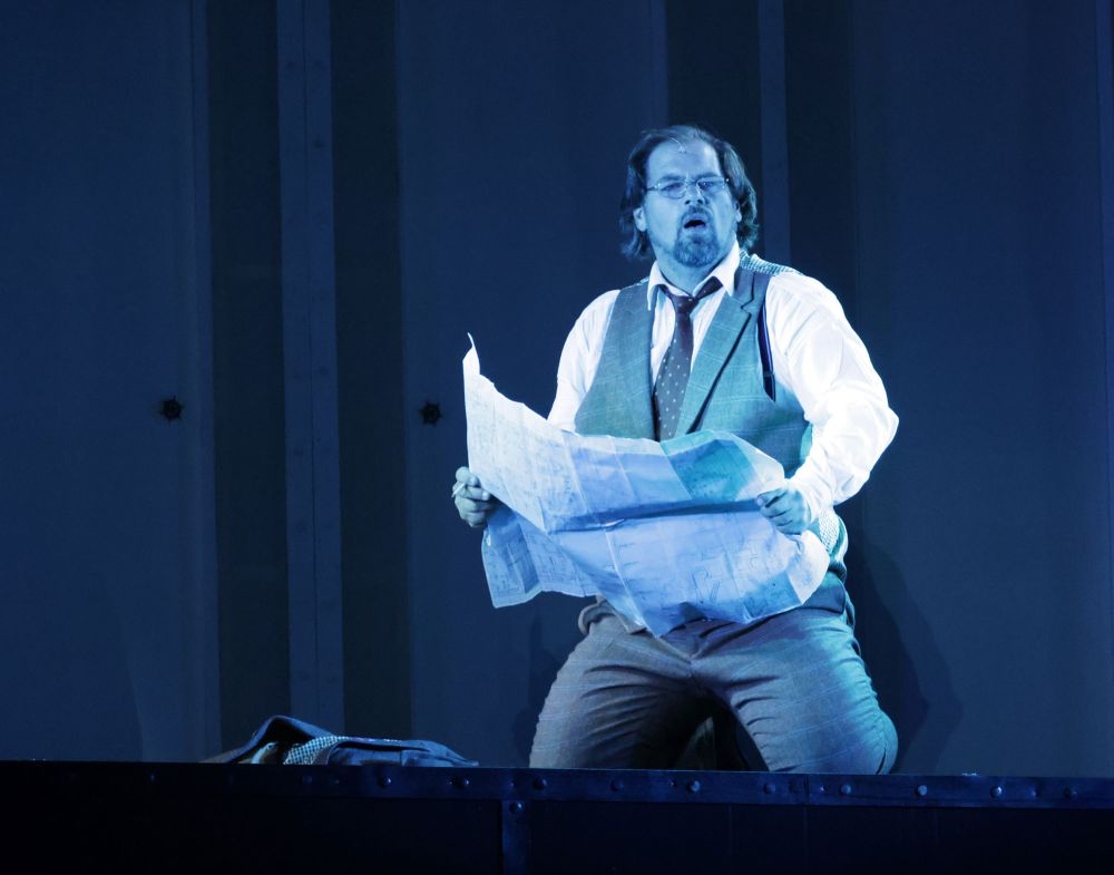 Schauspieler in blauem licht auf der Bühne mit einer Zeitung in der Hand